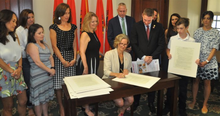 La ejecutiva del condado Laura Curran firma la ordenanza de seguridad del restaurante del legislador Josh Lafazan sobre alergia alimentaria en la ceremonia
